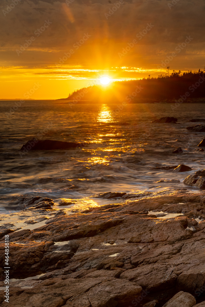 Obraz premium Acadia National Park, ME - USA - Oct. 13, 2021: Sunset vertical view of Ship Harbor at Acadia National Park in the Fall. Sunburst reflecting warm orange and yellow reflections on the surf.