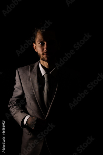 A young businessman in a smart gray suit looking at the camera with moody lighting that casts half of him into shadow