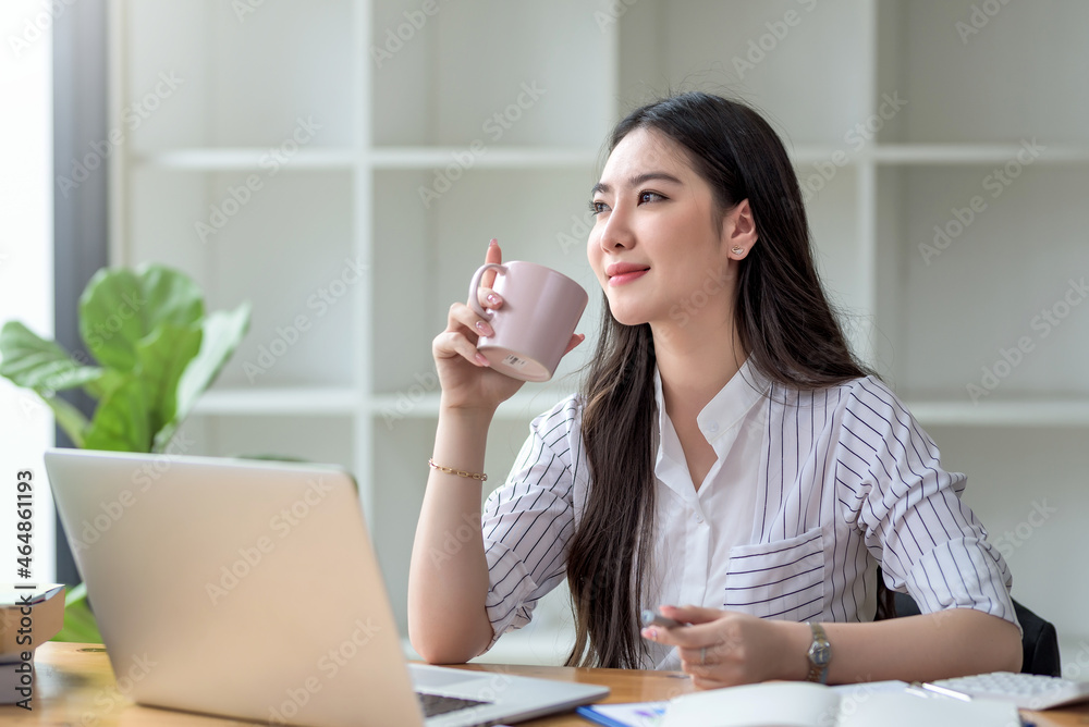 Beautiful young Asian businesswoman smiling holding a coffee mug and laptop working at the office. Beautiful young Asian businesswoman smiling holding a coffee mug and laptop working at the office.