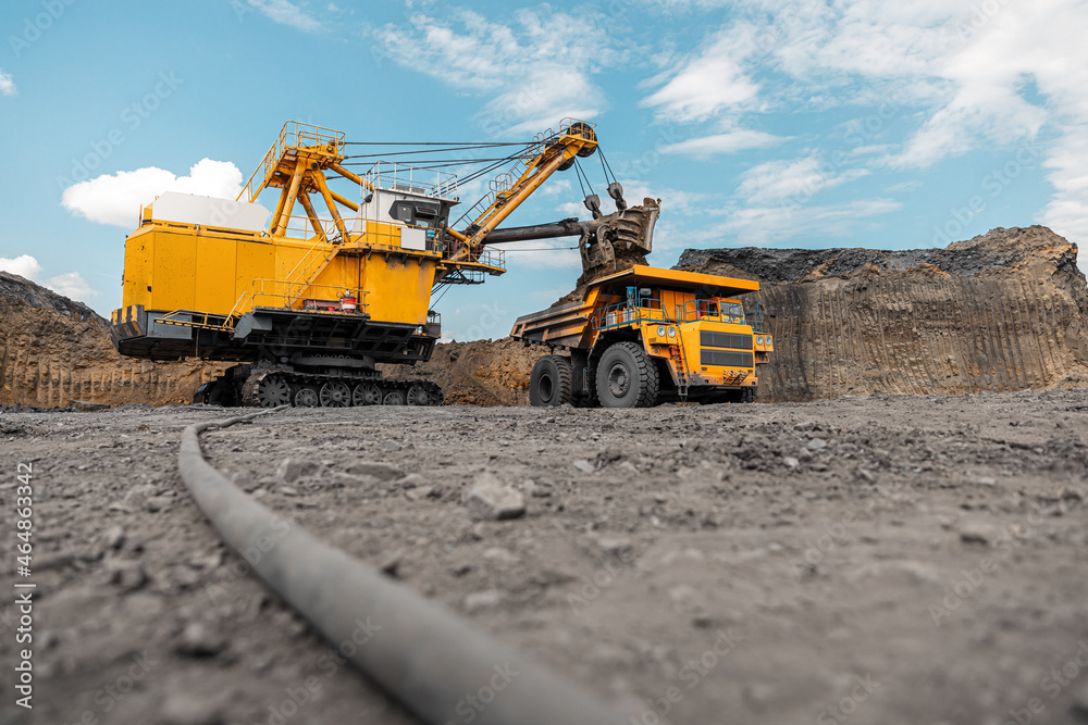 Large quarry dump truck. Big yellow mining truck at work site. Loading coal into body truck. Production useful minerals. Mining truck mining machinery to transport coal from open-pit production Large quarry dump truck. Big yellow mining truck at work site. Loading coal into body truck. Production useful minerals. Mining truck mining machinery to transport coal from open-pit production