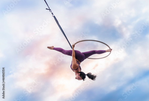 Asian beautiful woman doing aerial hoop or aerial ring practice outdoor. Woman hanging in aerial ring in the bright sky © somchairakin