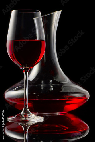 A glass of red wine and decanter on a glossy table.