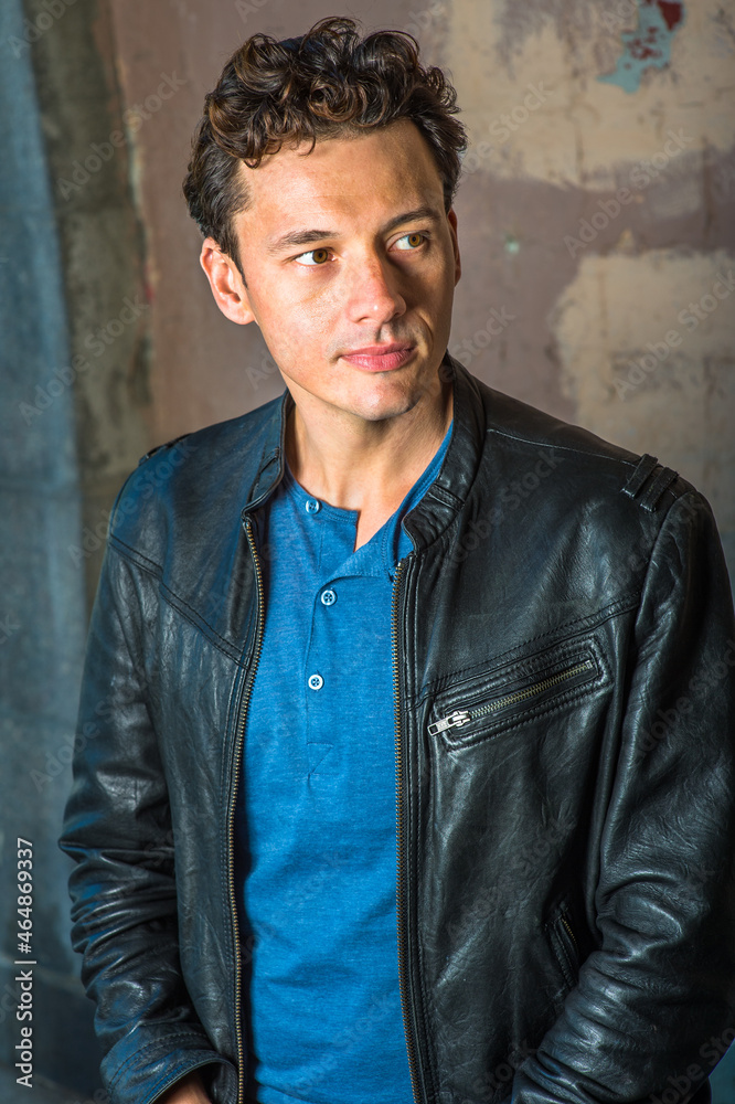 Dressing in a black leather jacket, a blue shirt, a young handsome guy is thoughtfully looking away..