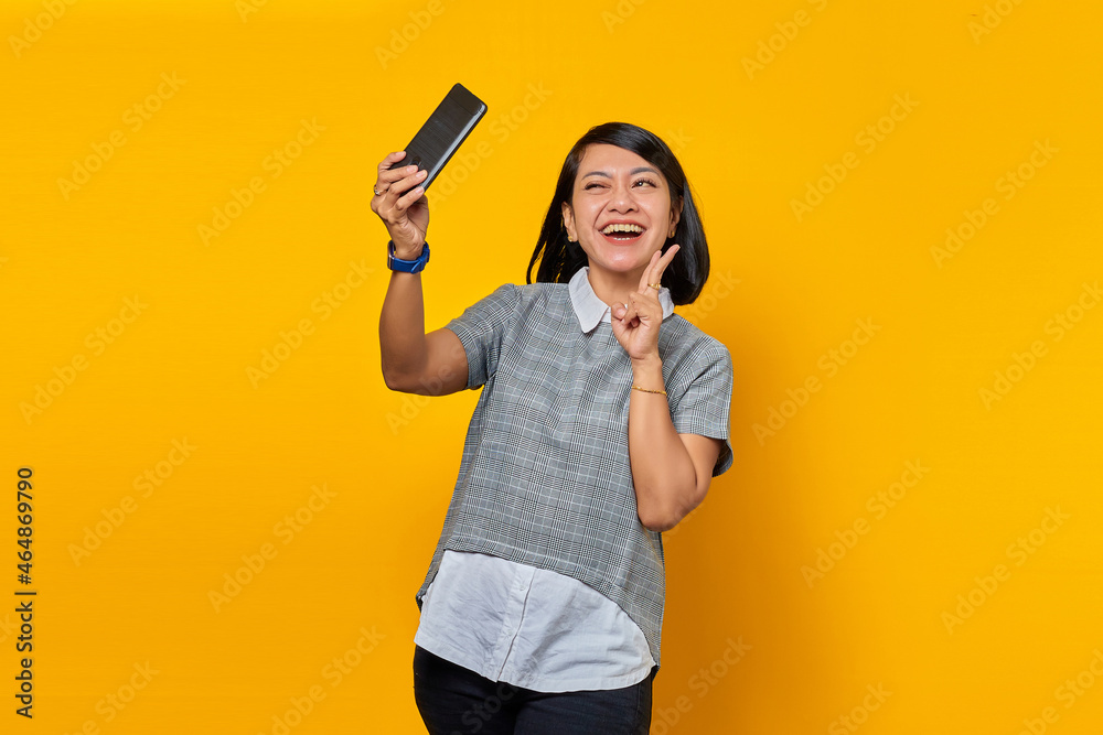 Portrait of cheerful young Asian woman using mobile phone take selfie make peace sign Portrait of cheerful young Asian woman using mobile phone take selfie make peace sign