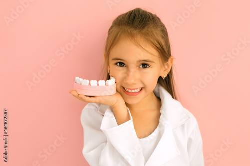 Cute charming little dentist holds model jaws in the palm of his hand close to face, smiling broadly, showing his perfect teeth. Children's Dentistry - tooth fairy. National dentist s day photo