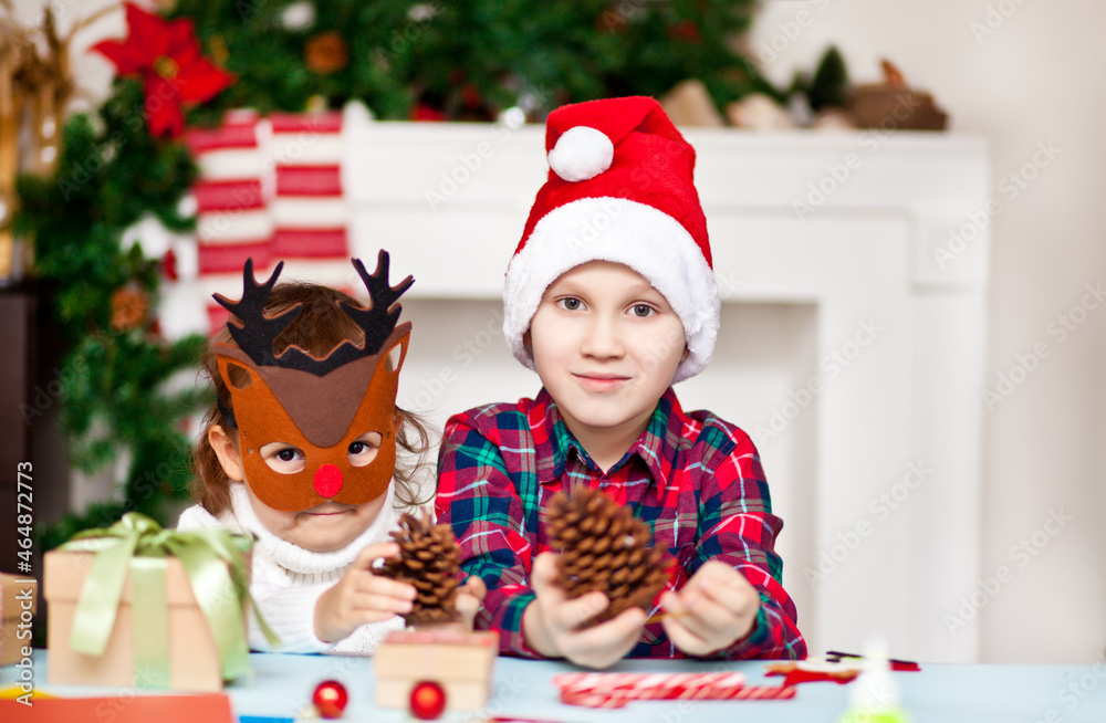Funny girl and boy in a Christmas deer mask and Santa cap holding pine cones