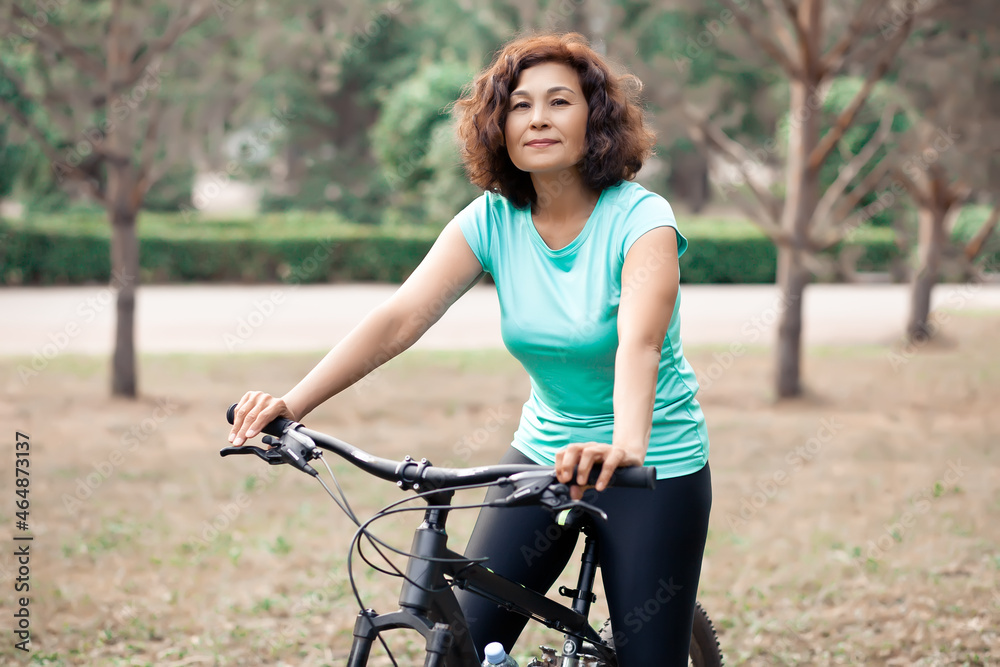 Obraz premium Middle age senior woman on bike cycle ride in countryside park outdoor