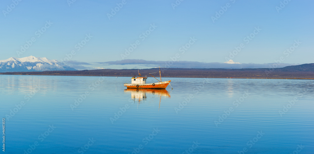 Fjord with small fishing boat and snow covered mountains in south Chile
