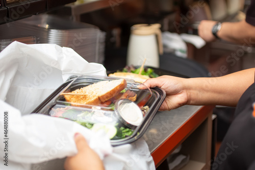 A view of an employee preparing to pack a food to-go container, in a restaurant kitchen setting.