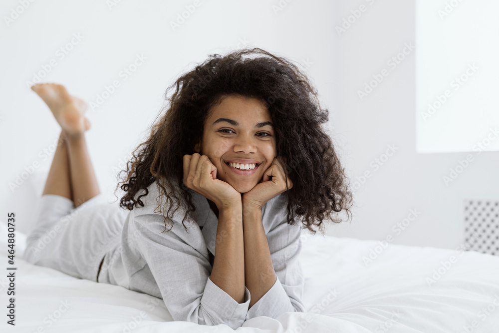 Cheerful young afro american woman lying on bed, looking at camera Cheerful young afro american woman lying on bed, looking at camera