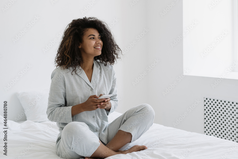 African american woman sitting with smartphone on bed African american woman sitting with smartphone on bed