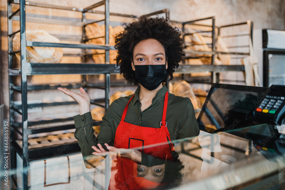 Beautiful African American female worker with protective face mask working in bakery.