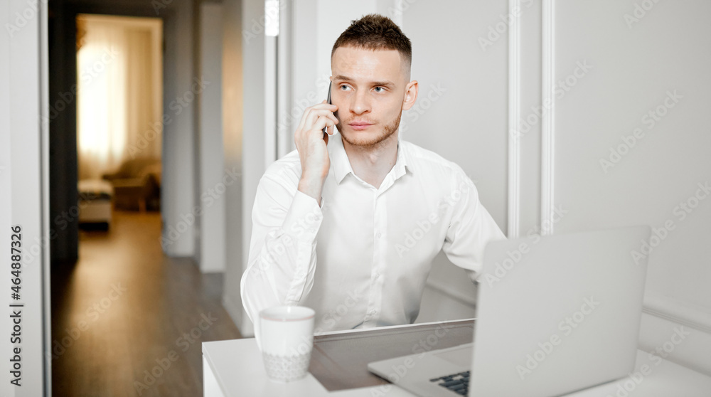 A young man works in the kitchen, talks on the phone, working at a laptop A young man works in the kitchen, talks on the phone, working at a laptop