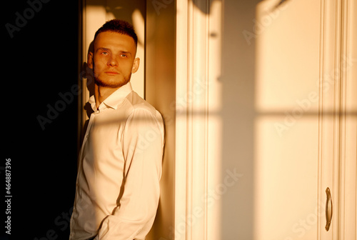 a young man looks at sunset through the window on him falls shadow