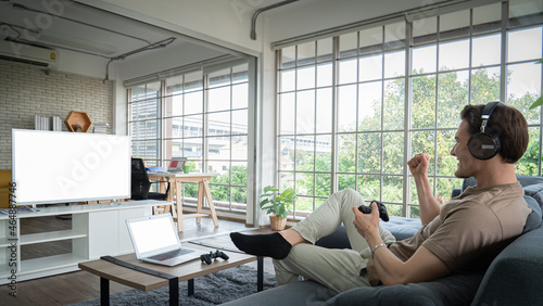 Concept, game or e-sport. Young Caucasian man, white, holding, joystick, game console, looking at screen. There are headphones around the neck. young men playing games in the living room of the house