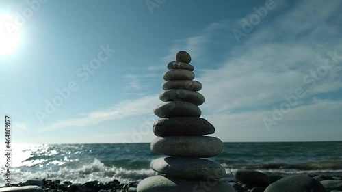 Balanced pebble pyramid swing in the wind on the beach, waves background. Zen stones on the sea beach, meditation, harmony, calmness, balance, concept