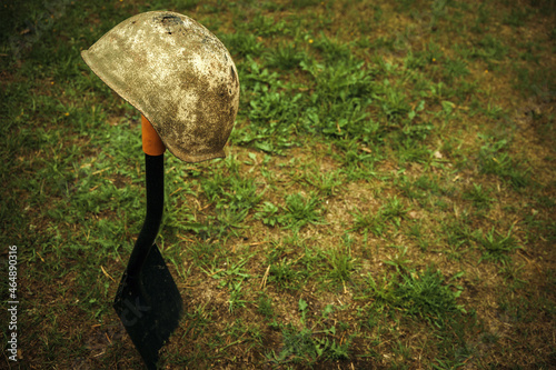 A rusty soldier's helmet hangs on the handle of a shovel stuck in the ground. Search for missing soldiers. Military excavations. Memory watch. Burial of warriors. photo