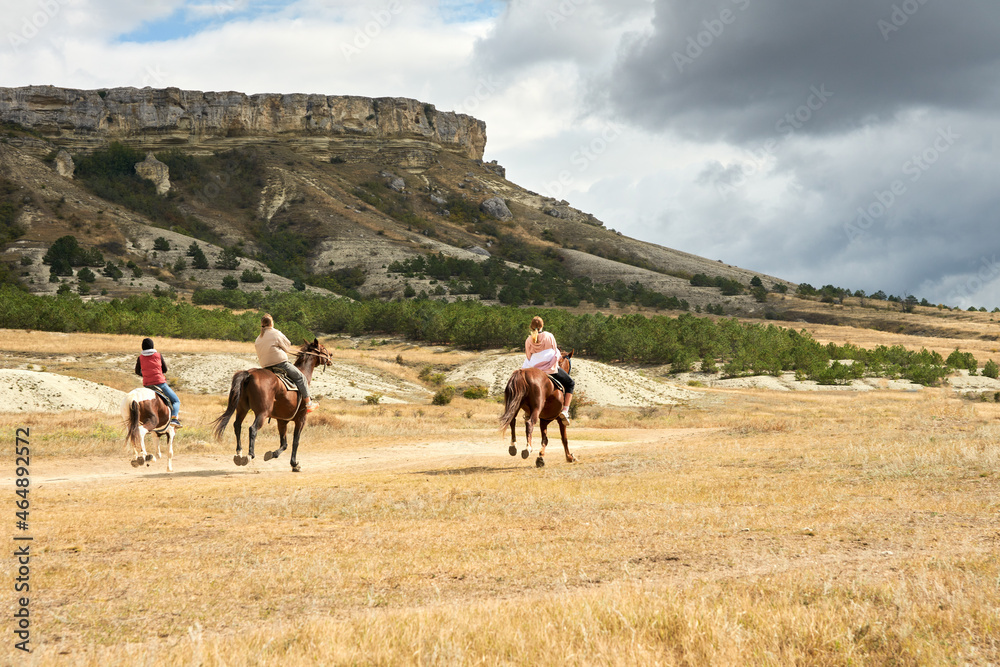  A group of three people rides horses on the prairie along the Rocky Mountains. Selective focus. Copy space.