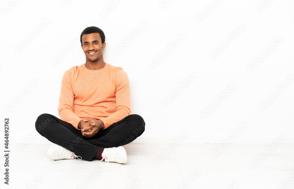 African American man sitting on the floor over isolated copyspace background posing with arms at hip and smiling