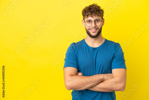 Young handsome caucasian man isolated on yellow background keeping the arms crossed in frontal position