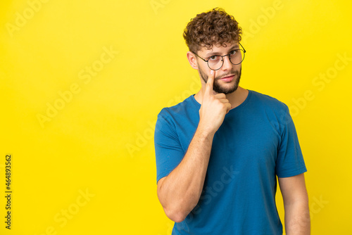 Young handsome caucasian man isolated on yellow background showing something