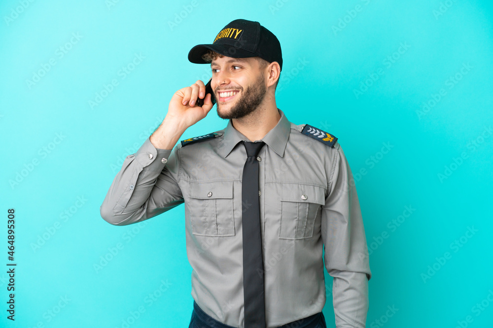 Young security man isolated on blue background keeping a conversation with the mobile phone Young security man isolated on blue background keeping a conversation with the mobile phone
