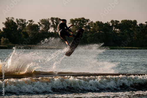 Great view of dynamic guy holding rope and jumping high with wakeboard over water photo