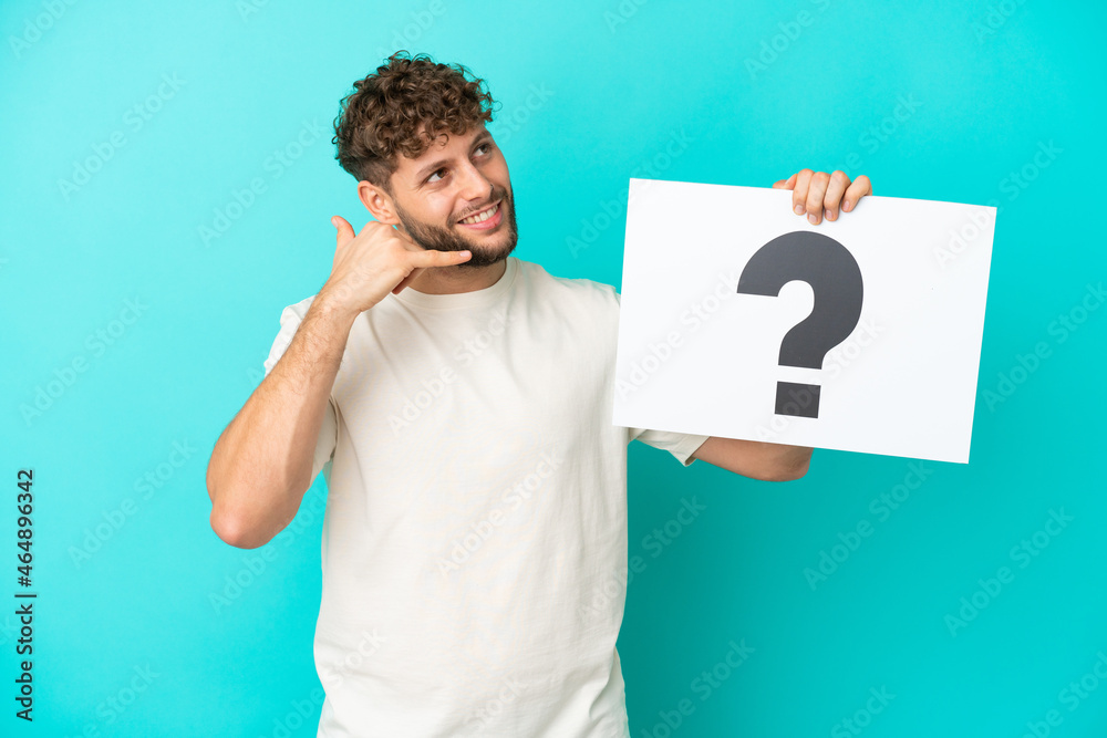 Young handsome caucasian man isolated on blue background holding a placard with question mark symbol and doing phone gesture Young handsome caucasian man isolated on blue background holding a placard with question mark symbol and doing phone gesture