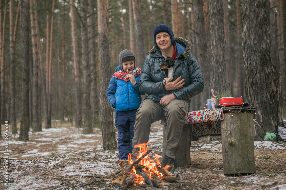 Happy family near the fire on a walk outdoors in sunny winter forest, Christmas holidays, father and son play together Happy family near the fire on a walk outdoors in sunny winter forest, Christmas holidays, father and son play together