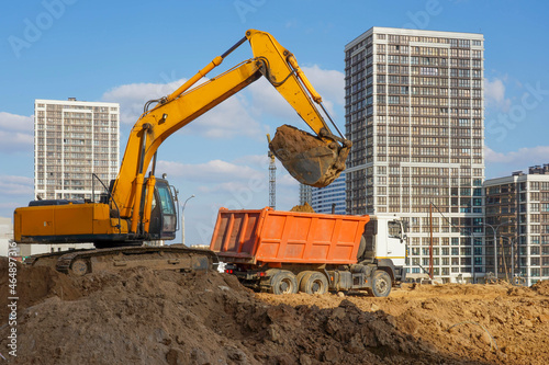 Photo of an excavator and a truck at the construction site of multi-storey buildings in the city