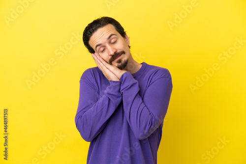 Young caucasian man isolated on yellow background making sleep gesture in dorable expression © luismolinero