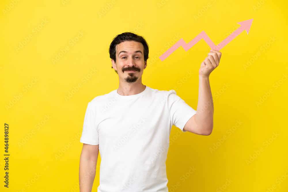 Young caucasian man isolated on yellow background holding a catching a rising arrow with happy expression Young caucasian man isolated on yellow background holding a catching a rising arrow with happy expression