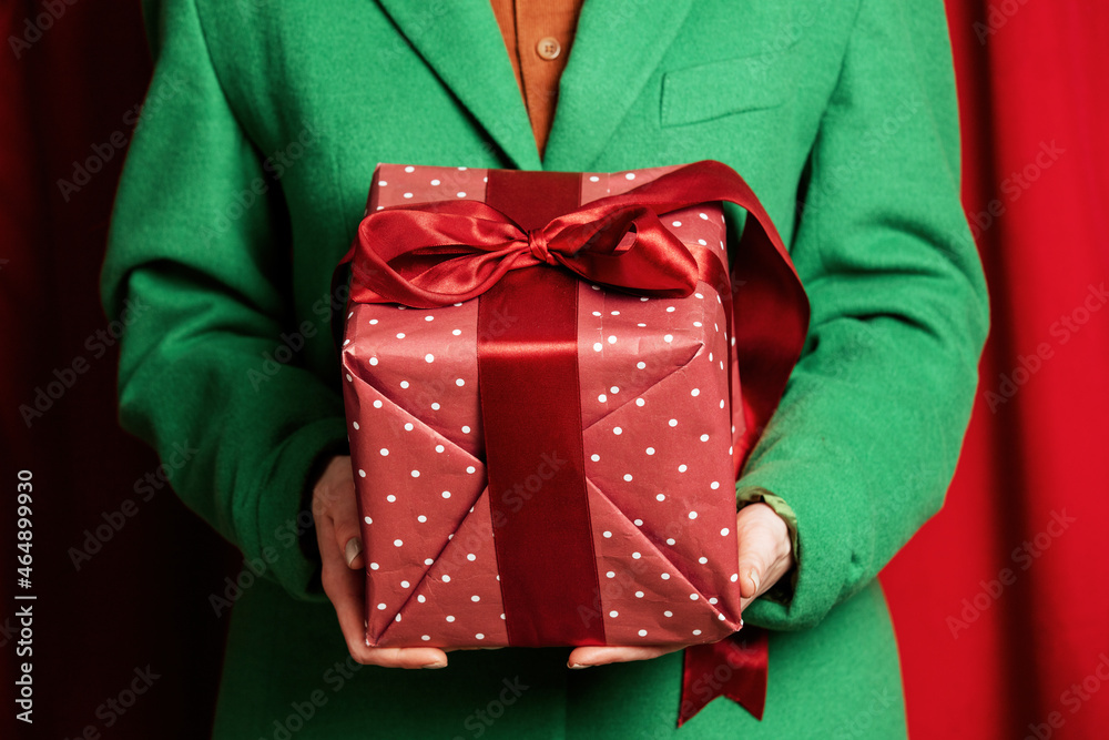 Woman in green jacket with holiday gift box on red curtains background Woman in green jacket with holiday gift box on red curtains background