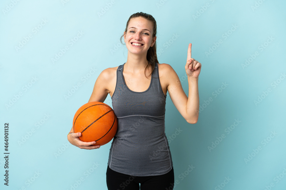 Young woman playing basketball isolated on blue background pointing up a great idea