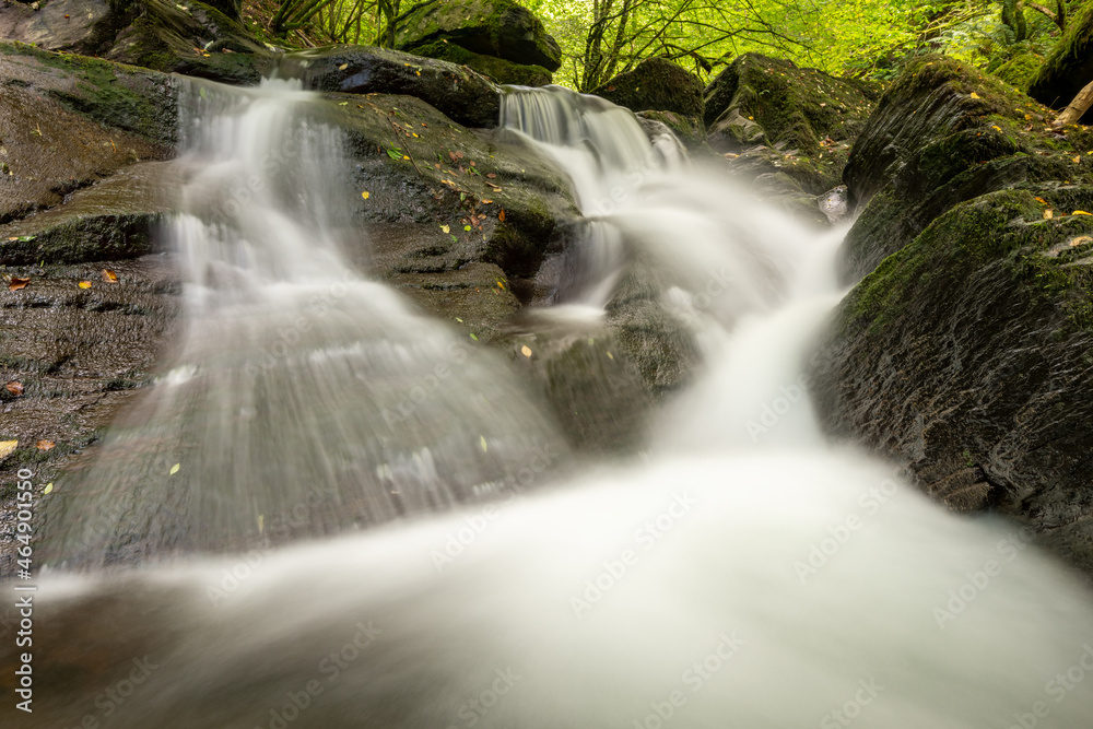 Obraz premium Long exposure of a waterfall on the Hoar Oak Water river flowing through the woods at Watersmeet in Exmoor National Park
