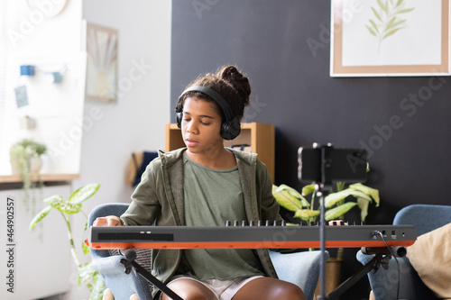 Photos Cute preteen biracial schoolgirl in headphones playing piano keyboard while sitt