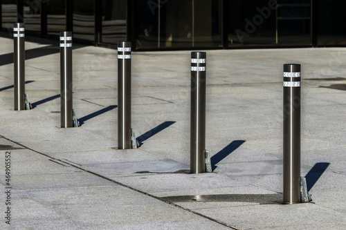 Steel parking posts to prevent vehicle access onto pavement. Five metal bollards with sunlight casting linear shadows. Rough cement surface. Dublin, Ireland