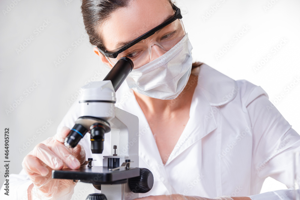 lab technician looks into the eyepiece of a microscope, a young female doctor lab technician looks into the eyepiece of a microscope, a young female doctor