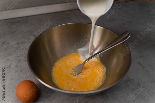White milk is poured into a bowl of beaten chicken eggs for an omelet
