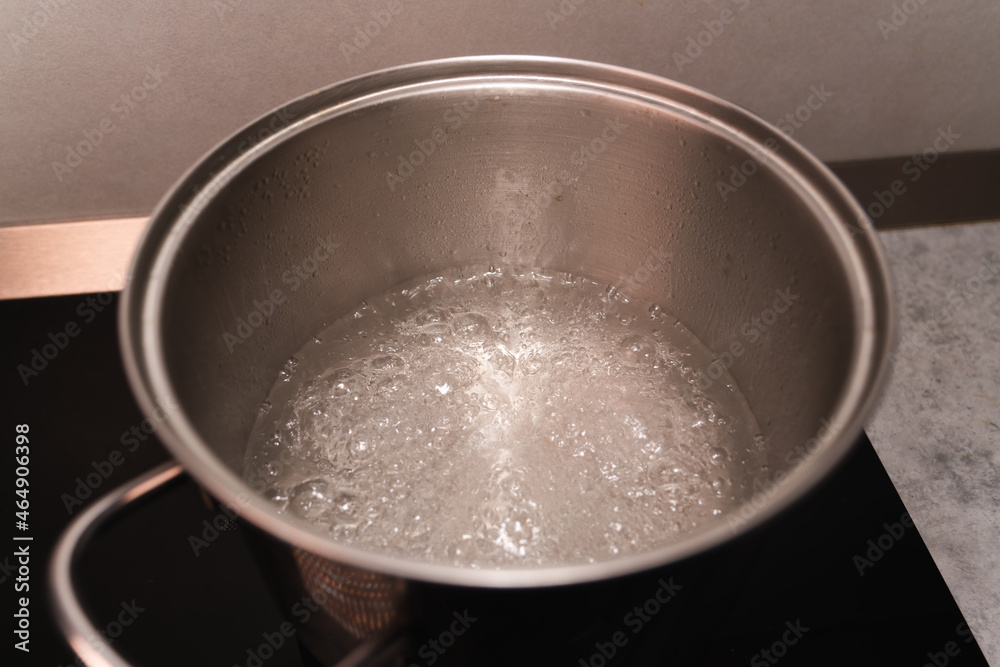 Boiling water in a metal saucepan on the black surface of an induction cooker Boiling water in a metal saucepan on the black surface of an induction cooker