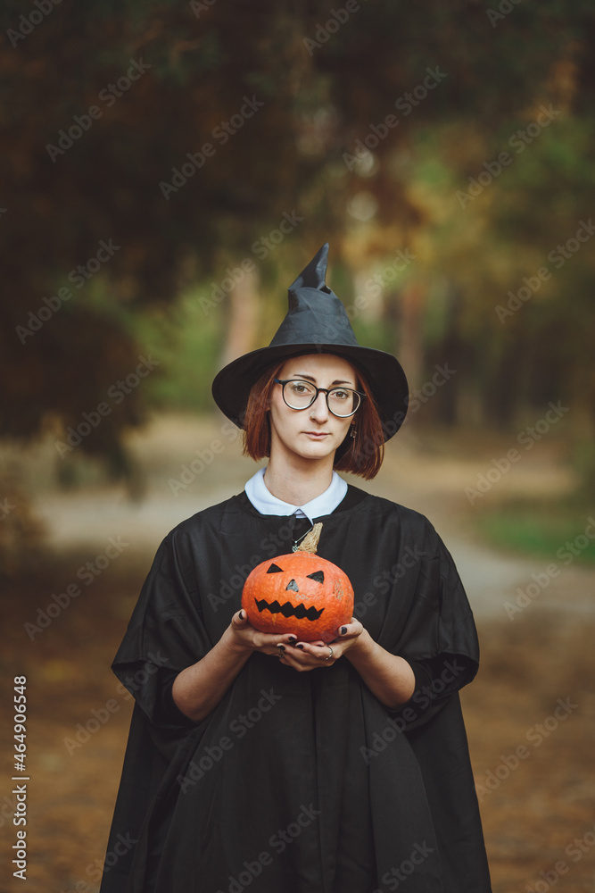 Halloween witch. Portrait of a girl in a hat and a witch costume with a pumpkin in the forest. Ready for the holiday