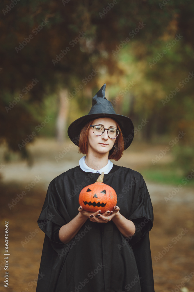 Halloween witch. Portrait of a girl in a hat and a witch costume with a pumpkin in the forest. Ready for the holiday