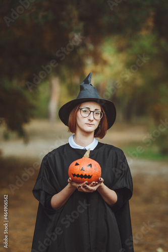 Obraz na płótnie Halloween witch. Portrait of a girl in a hat and a witch costume with a pumpkin in the forest. Ready for the holiday