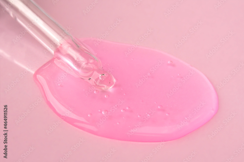 Pipette with fluid hyaluronic acid on pink background. Cosmetics and healthcare concept closeup. Dose of serum or retinol with air bubbles. Flat lay. Luxury gel or beauty product presentation in macro