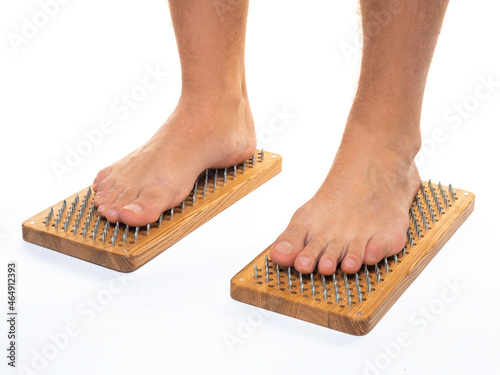 Male feet stand on a board with sharp nails over white background. Sadhu's board - practice yoga. Pain, trials, health, relaxation, cognition. Close-up.