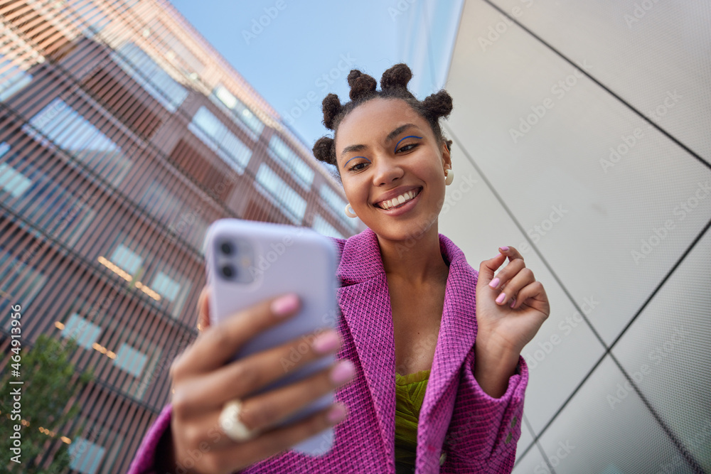 © wayhome.studio - Stylish lady with hairstyle dressed in fashionable pink jacket takes selfie on mobile phone for social networks poses against blurred city buildings smiles happily enjoys free time streams video © wayhome.studio - Stylish lady with hairstyle dressed in fashionable pink jacket takes selfie on mobile phone for social networks poses against blurred city buildings smiles happily enjoys free time streams video