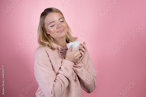 Enjoy a warming drink, a young sweet woman in a pink hoodie holds a mug