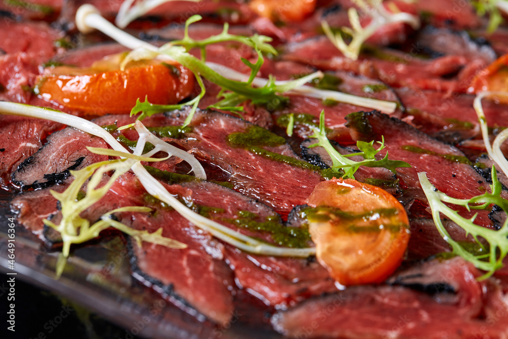 Closeup Beef carpaccio with pesto sauce and tomatoes on black table. Restaurant menu, natural and organic food concept. Closeup Beef carpaccio with pesto sauce and tomatoes on black table. Restaurant menu, natural and organic food concept.