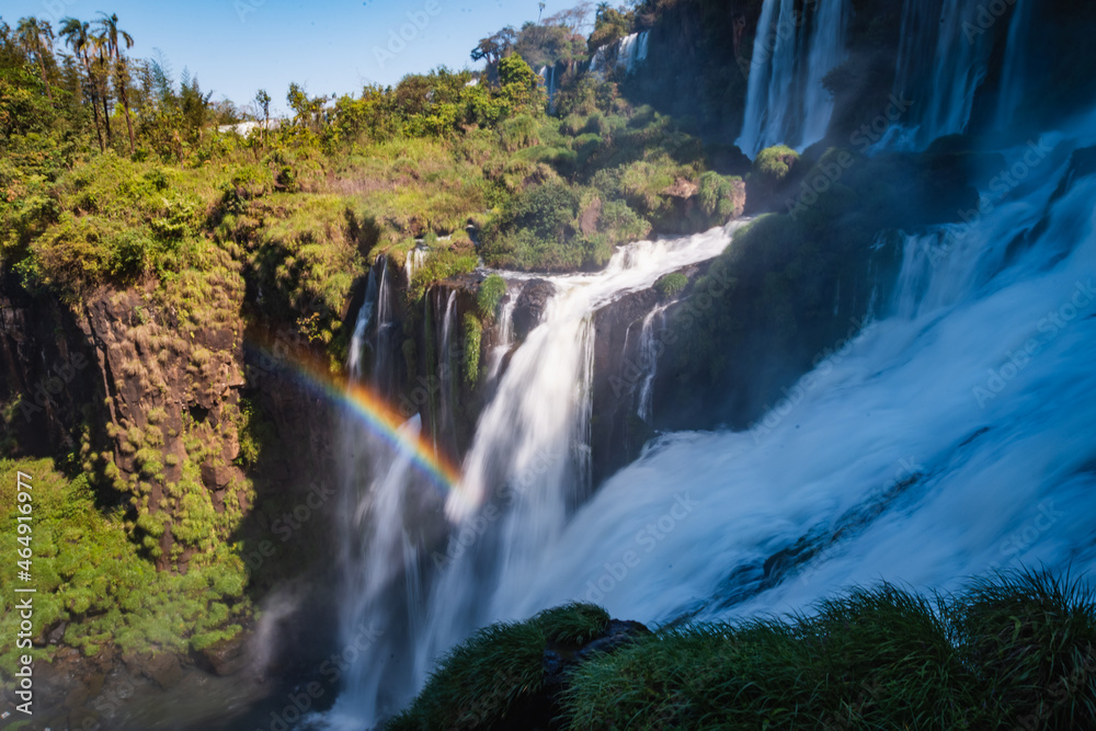 Naklejka premium a waterfall in the middle of the forest with blue sky in the background.