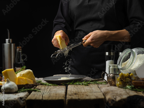 The chef grated cheese. Many ingredients for making pasta, pizza, focaccia, pie. Black background. Wooden texture. Bakery, pizzeria, restaurant, cooking blog, home cooking. photo